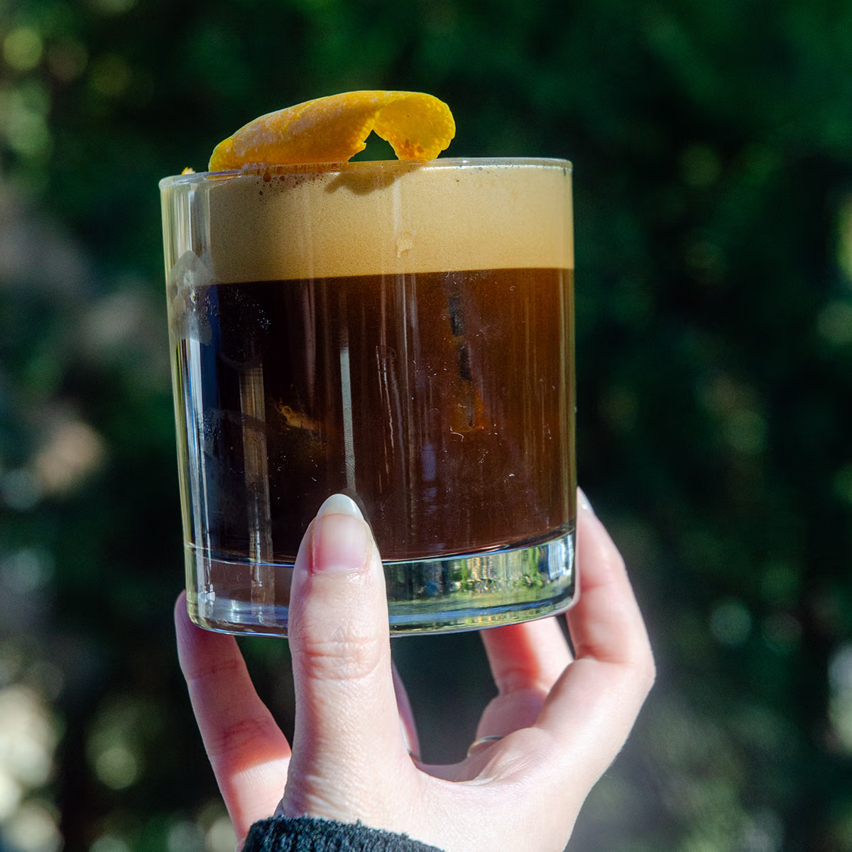 A hand holds up a Black Mountain Carajillo with an orange peel garnish