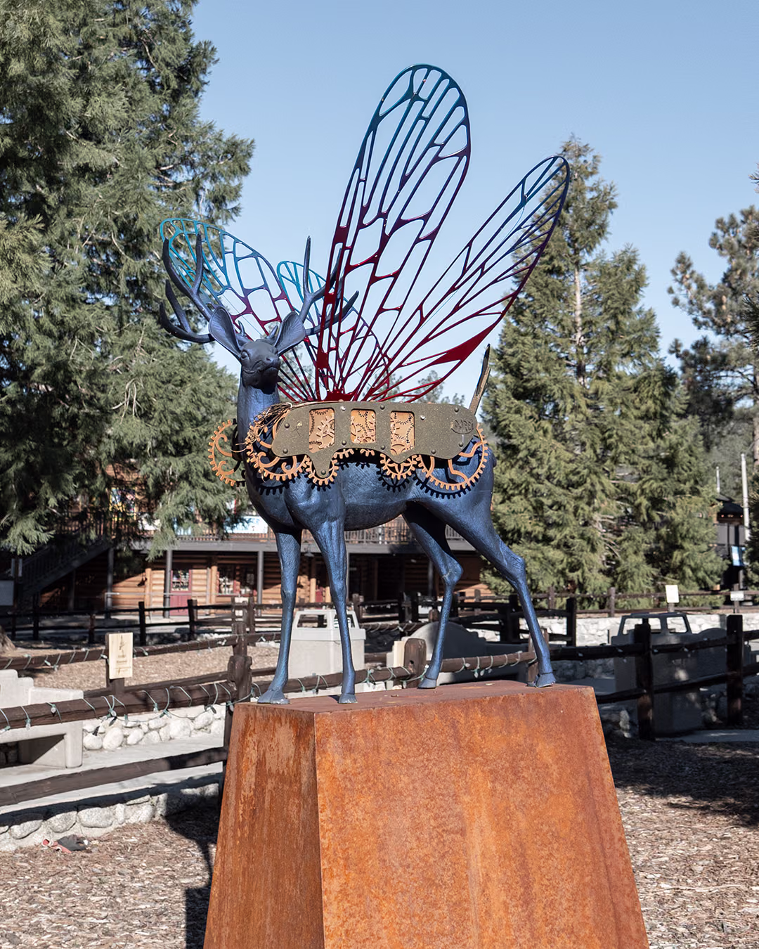 Metal deer sculpture with dragonfly wings and steampunk gears on a rusted steel plinth