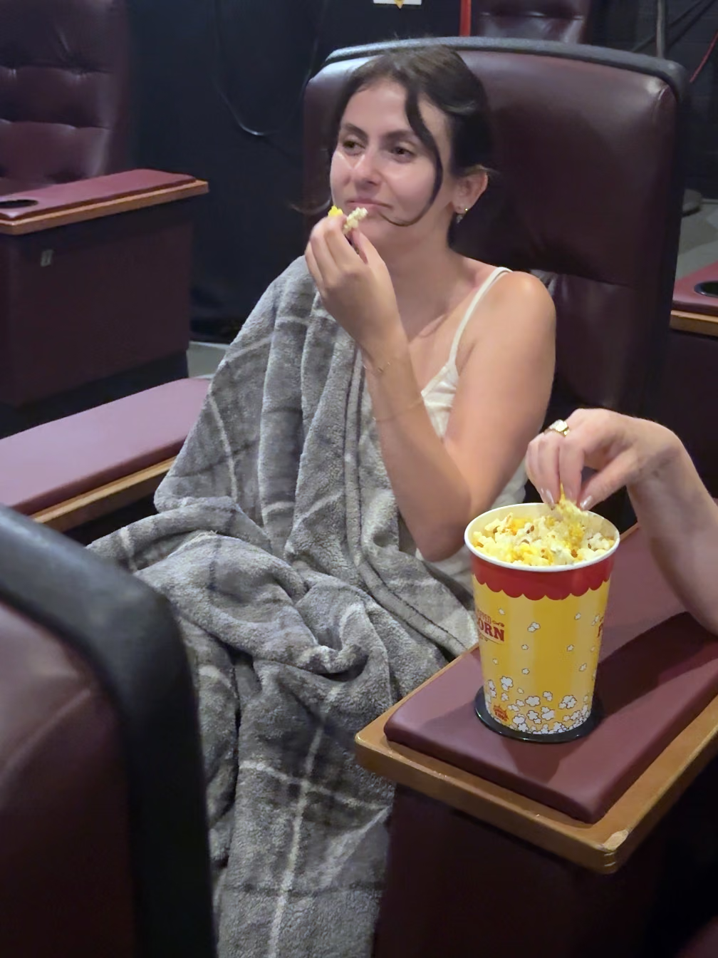 A moviegoer wrapped in a blanket eats popcorn in a leather recliner