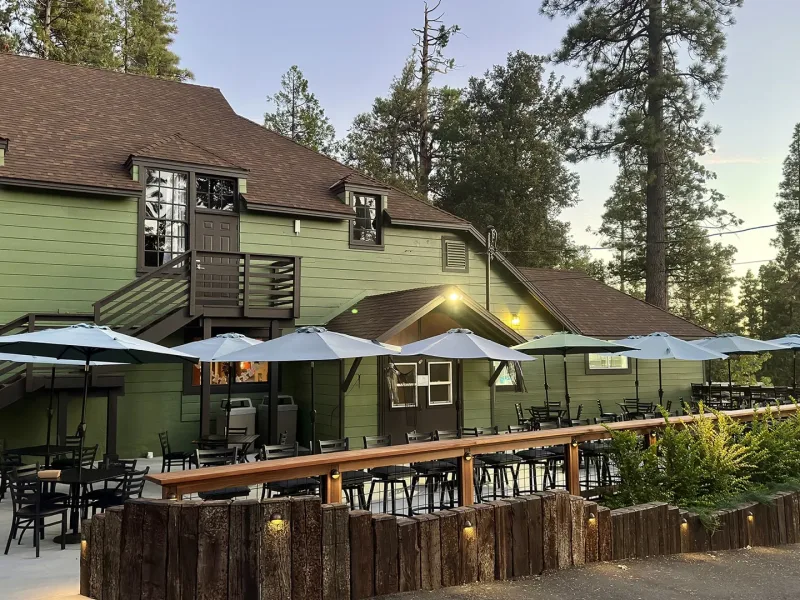 The Peak restaurant at dusk, its green building and patio umbrellas lit under tall pines